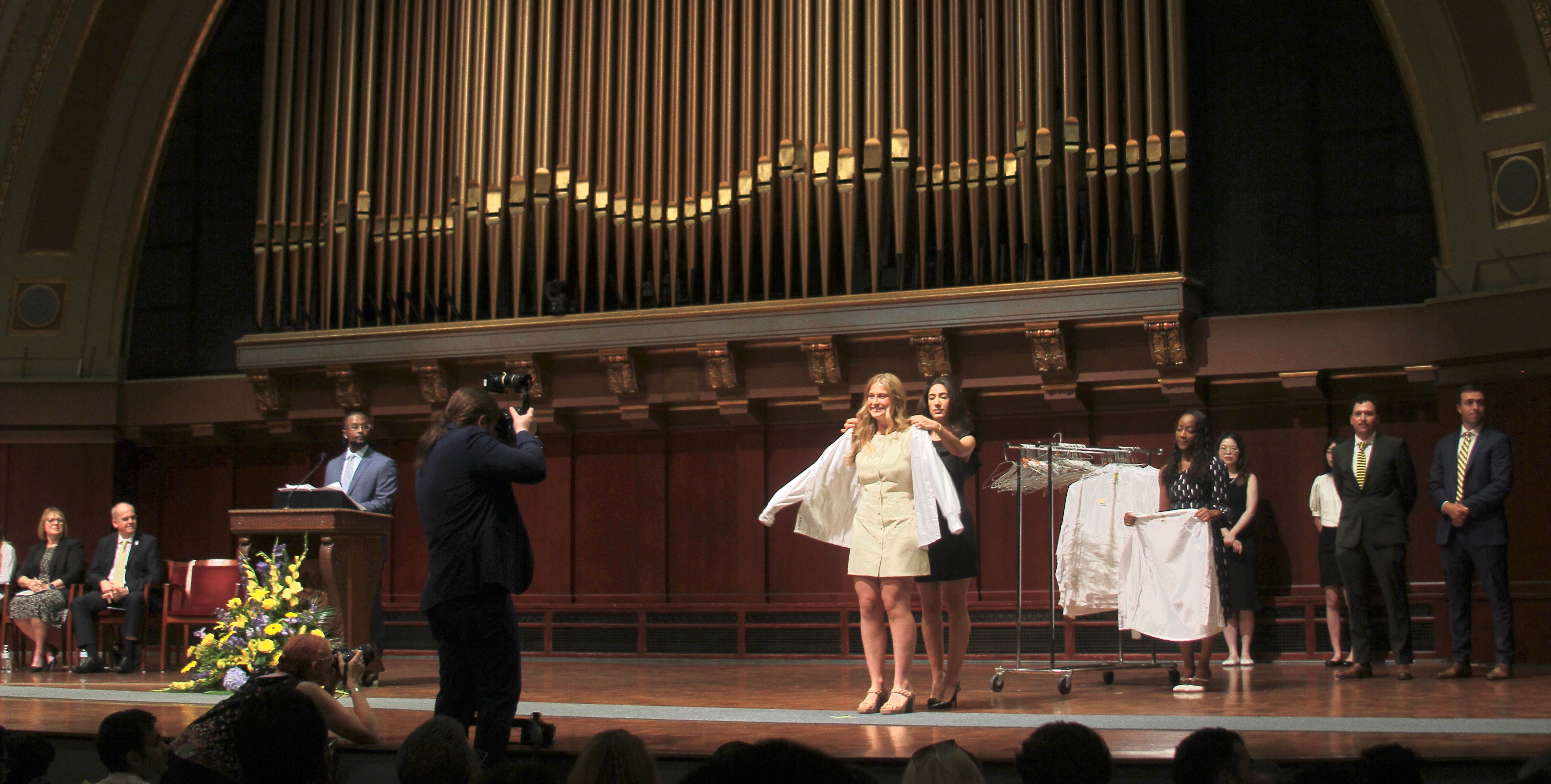 A School of Dentistry student is coated with a white coat on an auditorium stage.